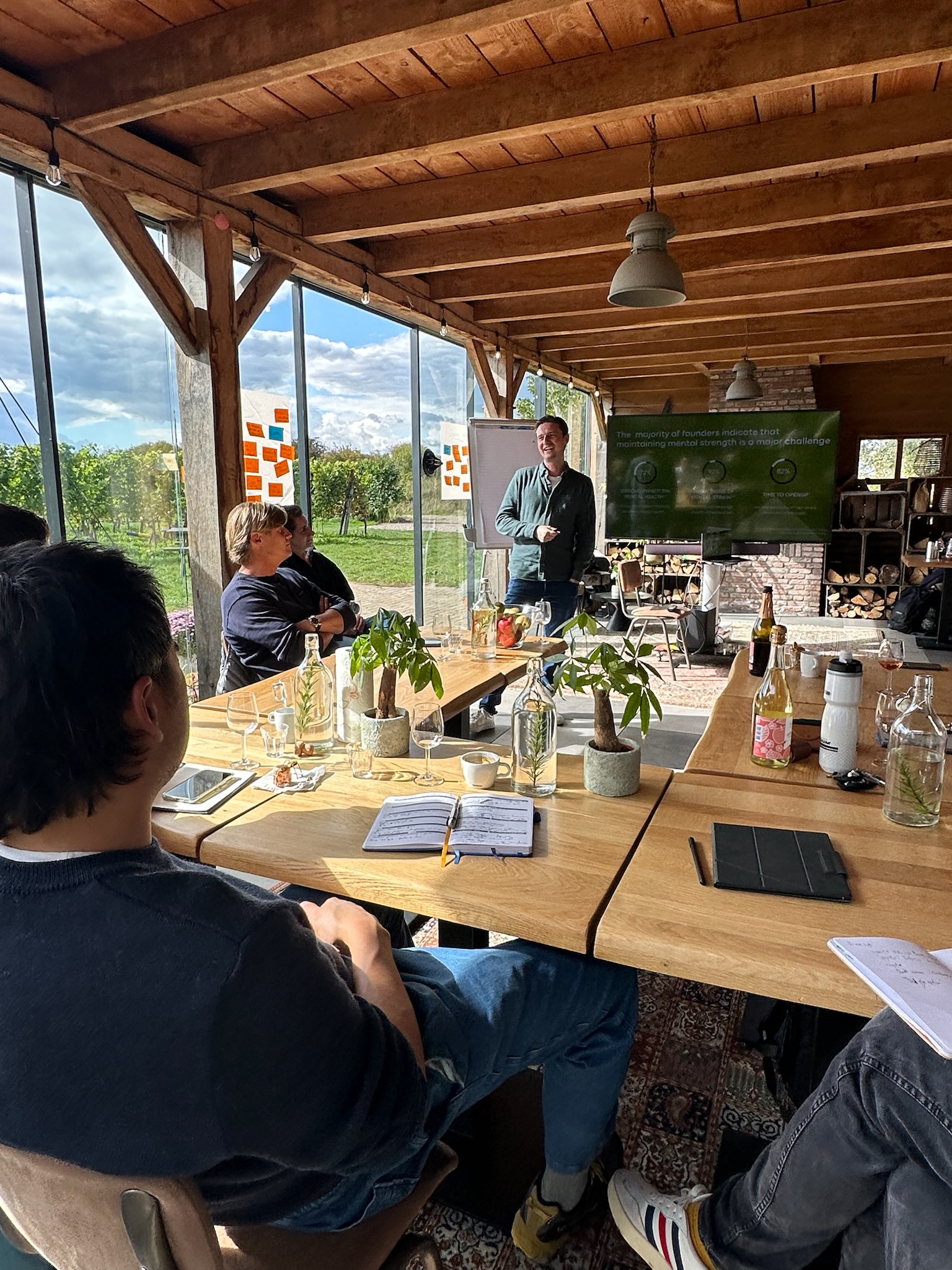 A Resilient Founders circle in session, long wooden table, daylight, greenhouse setting